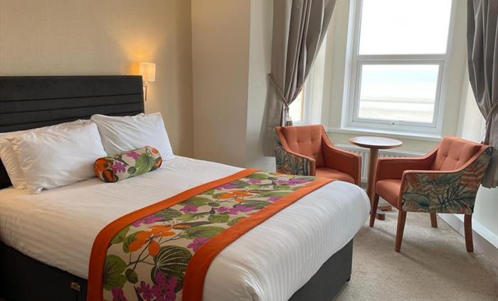 One of our superior double rooms, picture showing a King size bed with orange floral runner, 2 armchairs and a side table in the window overlooking th